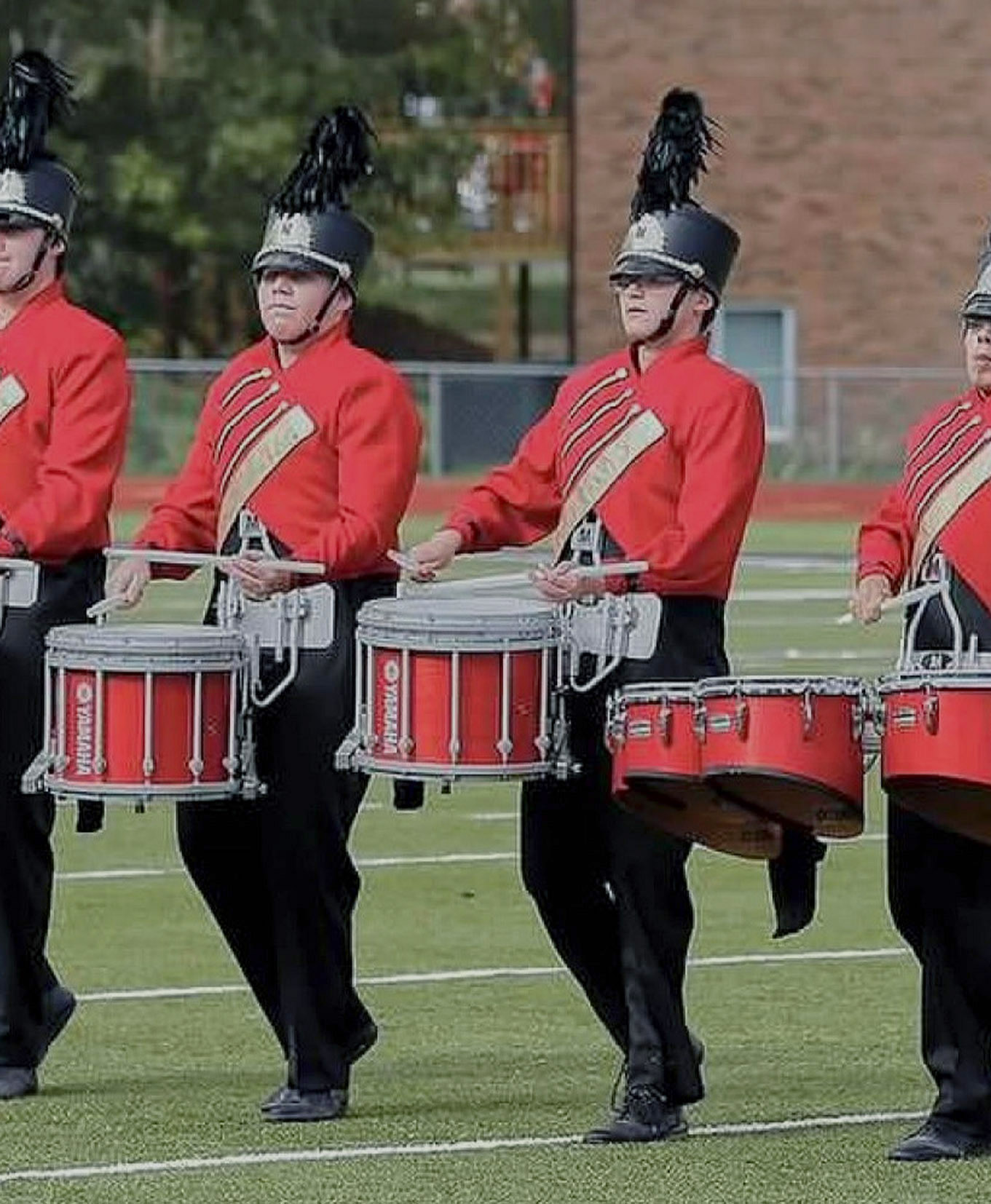 4 middle school age children in marching band uniforms playing in a drumline